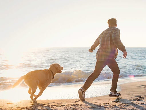 Muž so psom bežiaci po pláži
