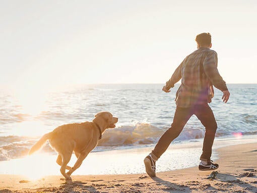 Muž so psom bežiaci po pláži